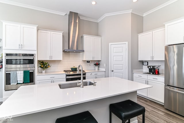 kitchen with stainless steel appliances, light countertops, a center island with sink, and wall chimney exhaust hood