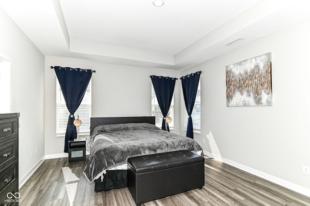 bedroom featuring baseboards, visible vents, a tray ceiling, and wood finished floors