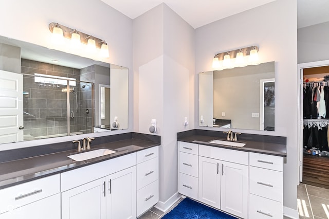 bathroom with a stall shower, two vanities, a sink, and a spacious closet