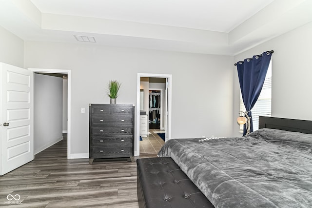 bedroom featuring ensuite bath, baseboards, a raised ceiling, and dark wood-type flooring