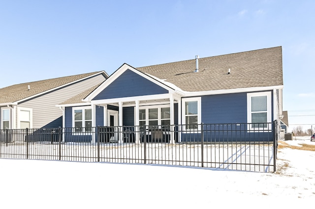 snow covered rear of property featuring roof with shingles, fence, and a sunroom