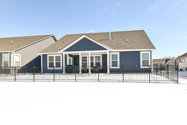 back of property with a fenced front yard and roof with shingles