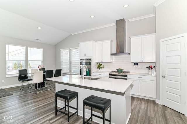 kitchen with light countertops, wall chimney range hood, a center island with sink, and white cabinetry