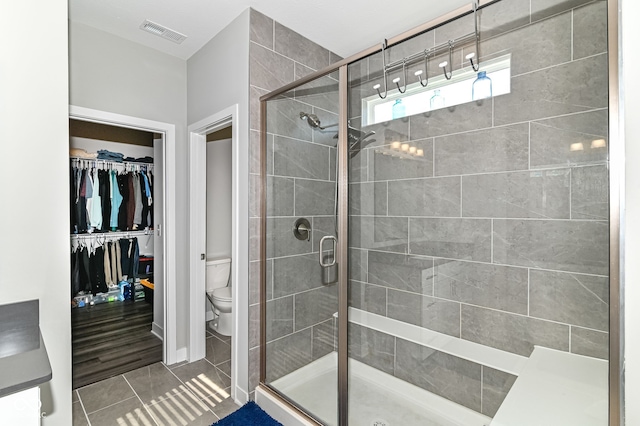 bathroom with toilet, visible vents, tile patterned floors, a stall shower, and a walk in closet