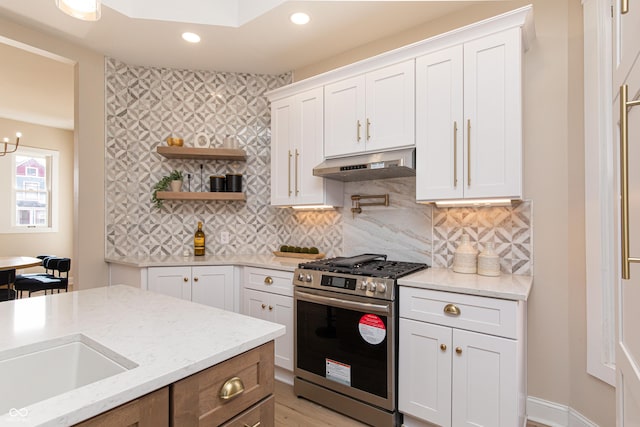 kitchen featuring light stone counters, backsplash, stainless steel gas range, and white cabinets