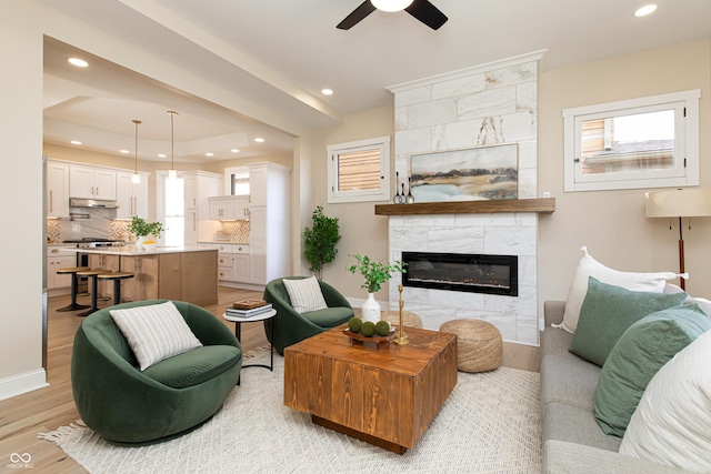 living room featuring plenty of natural light, light hardwood / wood-style floors, a tile fireplace, and ceiling fan