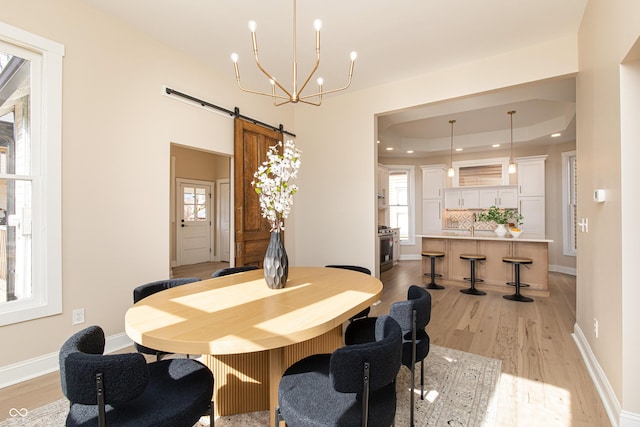 dining space featuring a notable chandelier, a tray ceiling, light hardwood / wood-style floors, and a barn door