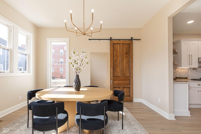 dining space featuring a barn door, a notable chandelier, and light hardwood / wood-style floors