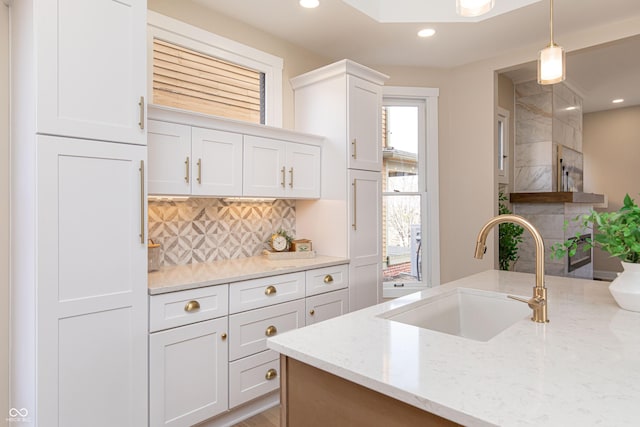 kitchen featuring hanging light fixtures, white cabinetry, sink, and light stone counters