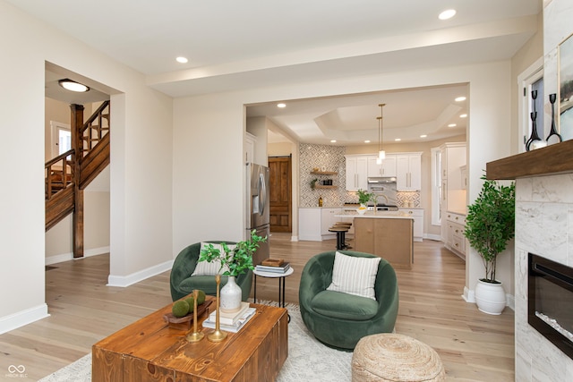 living room with a tray ceiling, a tiled fireplace, and light hardwood / wood-style flooring