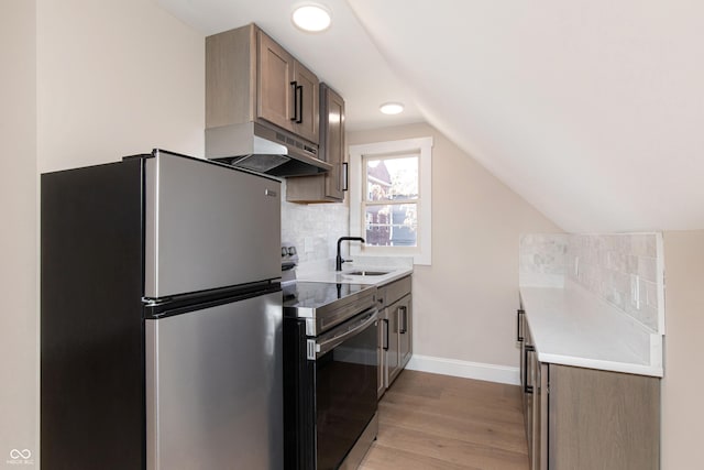 kitchen featuring lofted ceiling, sink, light wood-type flooring, appliances with stainless steel finishes, and decorative backsplash