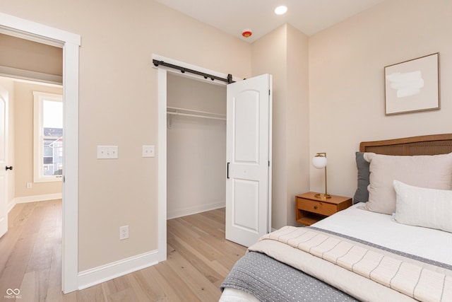 bedroom featuring a closet, a barn door, light hardwood / wood-style flooring, and a spacious closet