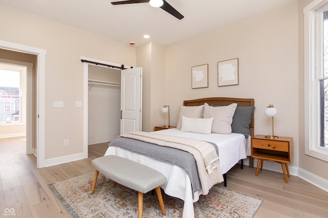 bedroom with ceiling fan, a barn door, a closet, and light wood-type flooring