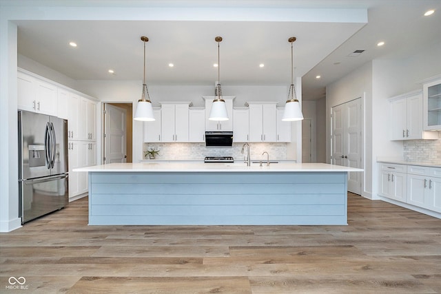 kitchen with hanging light fixtures, white cabinetry, a center island with sink, and stainless steel fridge