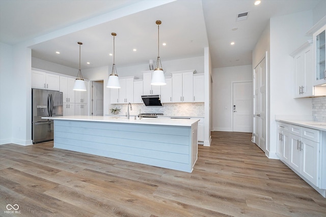 kitchen featuring light wood-type flooring, a kitchen island with sink, hanging light fixtures, stainless steel refrigerator with ice dispenser, and white cabinets