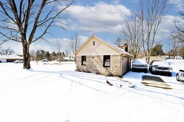 view of snowy exterior featuring a garage and brick siding