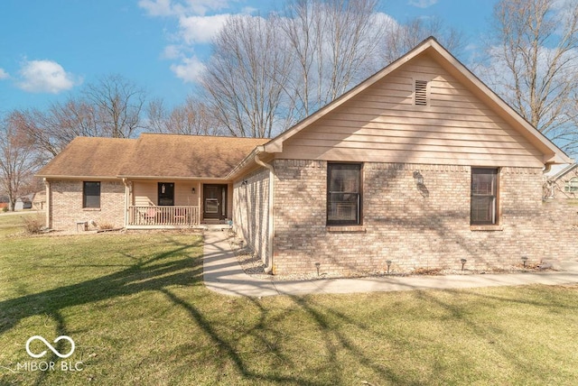 rear view of house with covered porch, brick siding, and a yard