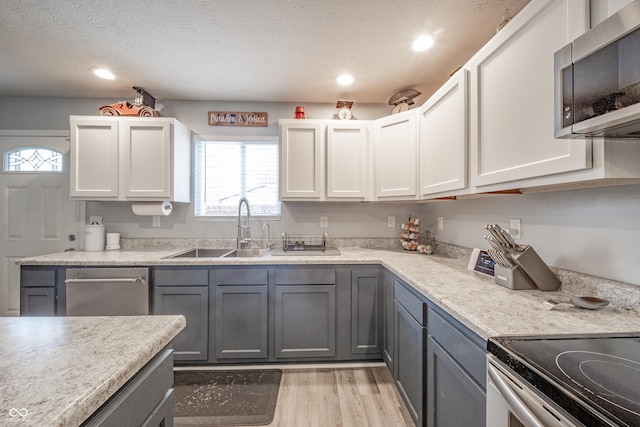 kitchen with gray cabinets, appliances with stainless steel finishes, white cabinetry, sink, and light wood-type flooring