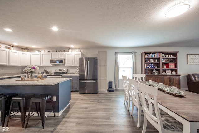 kitchen featuring appliances with stainless steel finishes, a breakfast bar area, white cabinets, a textured ceiling, and light hardwood / wood-style flooring