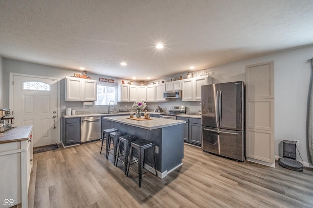 kitchen with sink, light hardwood / wood-style flooring, a kitchen island, stainless steel appliances, and a kitchen bar