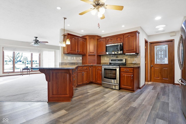 kitchen featuring tasteful backsplash, decorative light fixtures, dark stone countertops, stainless steel appliances, and hardwood / wood-style floors