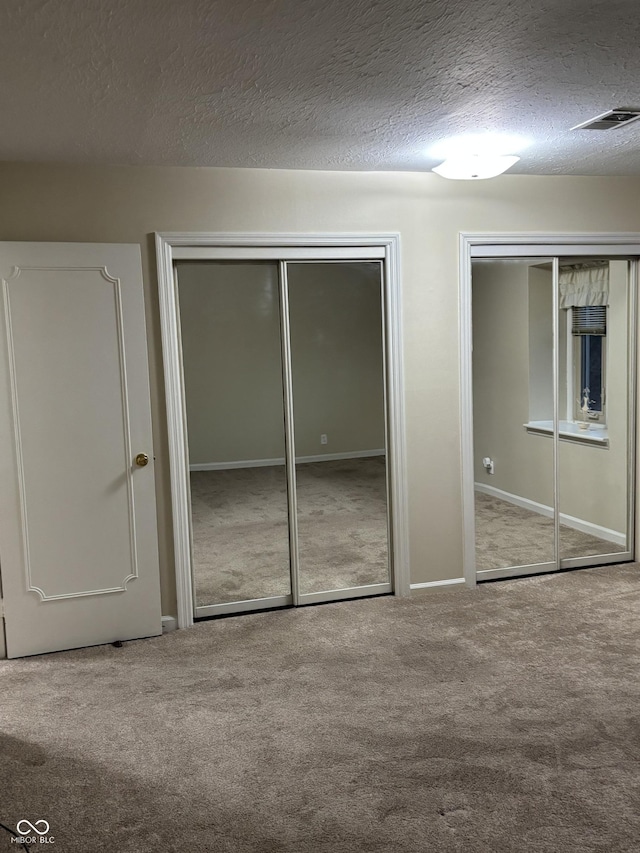 unfurnished bedroom featuring multiple closets, carpet flooring, and a textured ceiling