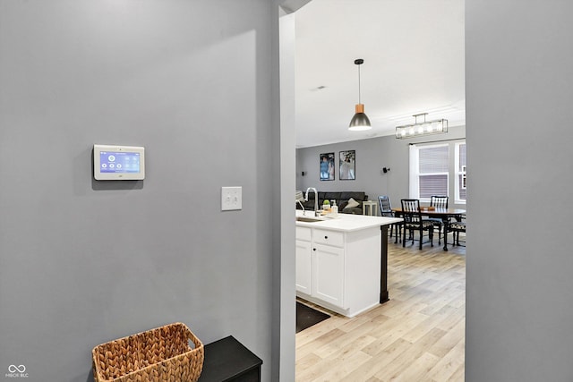 kitchen featuring white cabinetry, hanging light fixtures, sink, and light wood-type flooring