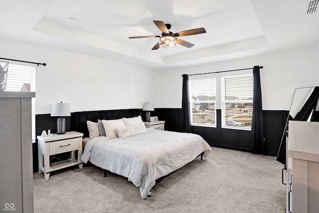 carpeted bedroom featuring multiple windows, a raised ceiling, and ceiling fan