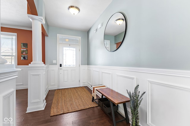 foyer entrance with ornate columns, dark wood-style floors, and a wainscoted wall