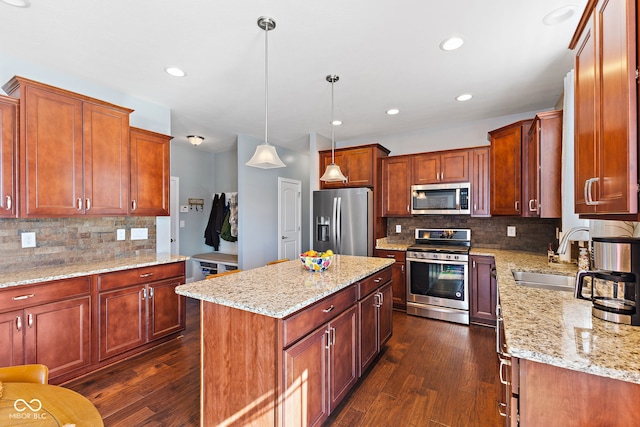 kitchen with a sink, a center island, appliances with stainless steel finishes, light stone countertops, and pendant lighting