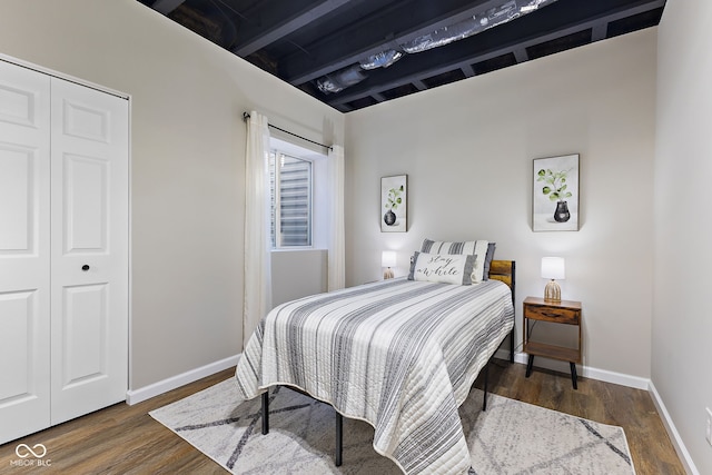 bedroom with a closet, dark wood-style flooring, beamed ceiling, and baseboards