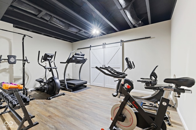 exercise room featuring a barn door, baseboards, and wood finished floors