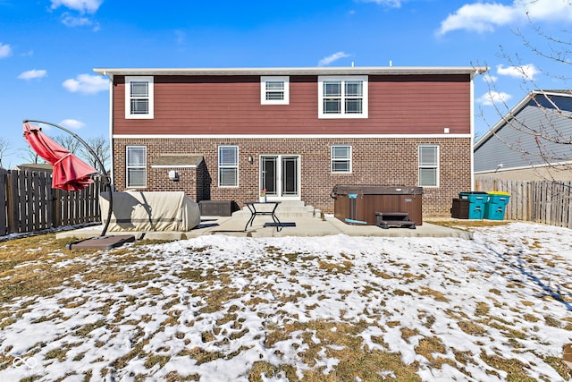 snow covered back of property with a hot tub, a fenced backyard, and brick siding