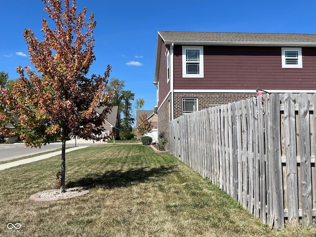 view of side of property with brick siding, fence, and a lawn