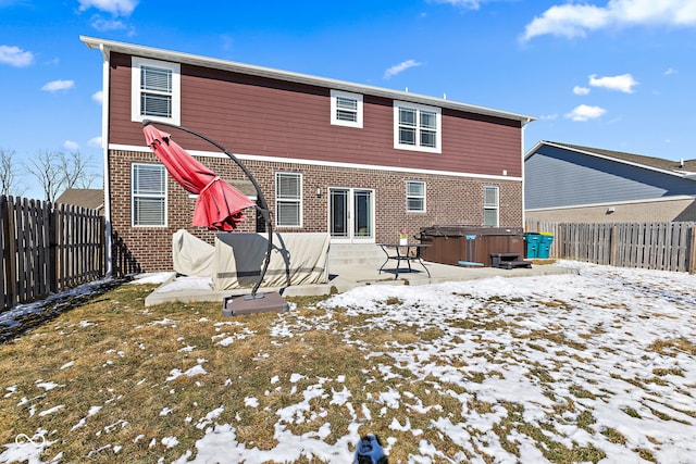 snow covered property featuring brick siding, a patio area, a fenced backyard, and a hot tub