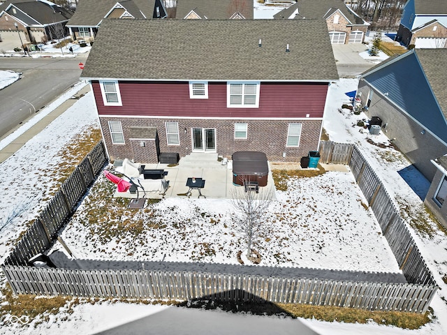 snow covered house featuring a fenced backyard, a residential view, and a jacuzzi