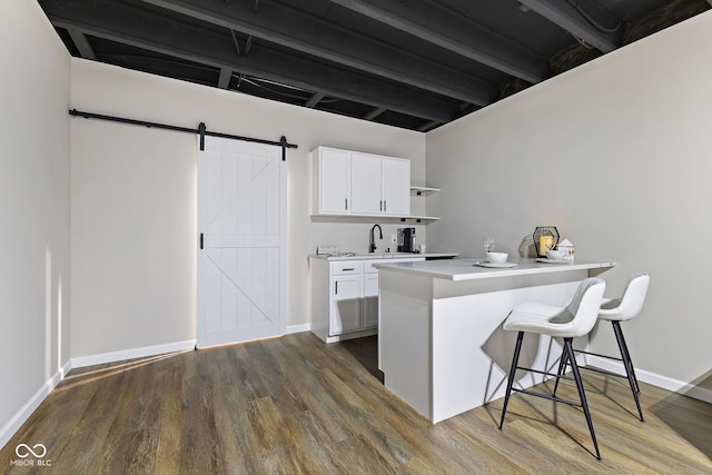 kitchen with a barn door, dark wood-type flooring, light countertops, a kitchen bar, and white cabinetry