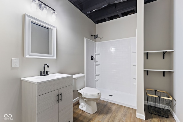 bathroom featuring toilet, vanity, wood finished floors, tiled shower, and baseboards