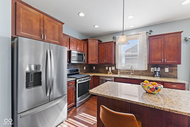 kitchen featuring dark wood-style flooring, a sink, appliances with stainless steel finishes, light stone countertops, and decorative light fixtures