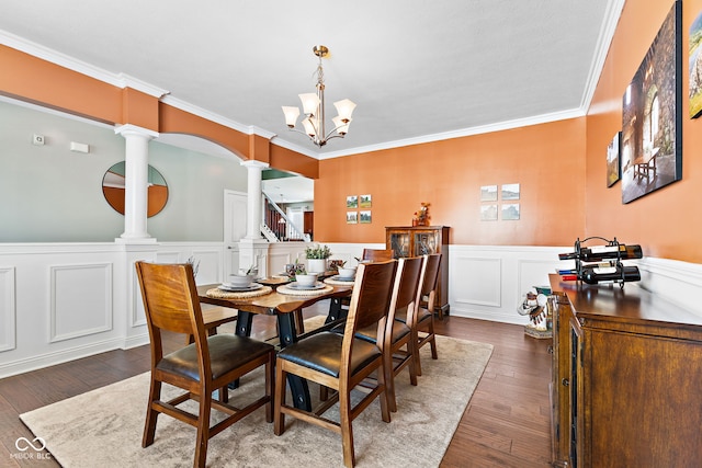 dining room with decorative columns, dark wood-style floors, a wainscoted wall, crown molding, and a notable chandelier