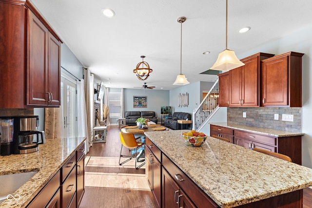 kitchen featuring a center island, light stone countertops, hanging light fixtures, and wood finished floors