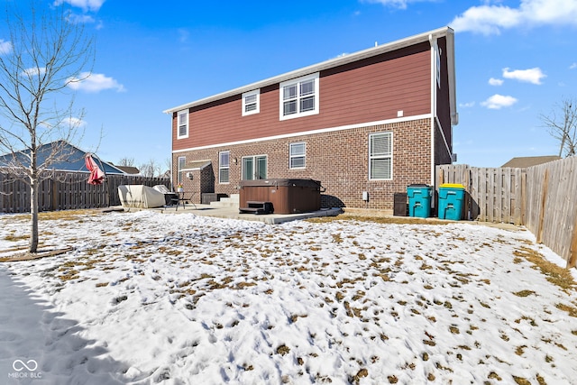 snow covered house with a fenced backyard, brick siding, and a hot tub