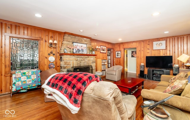 living room featuring a stone fireplace, recessed lighting, wood walls, wood finished floors, and ornamental molding