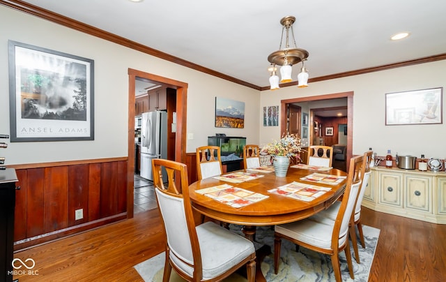 dining space with wood walls, dark wood-style flooring, wainscoting, and crown molding