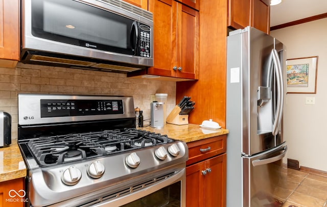 kitchen with baseboards, appliances with stainless steel finishes, brown cabinets, light stone counters, and backsplash