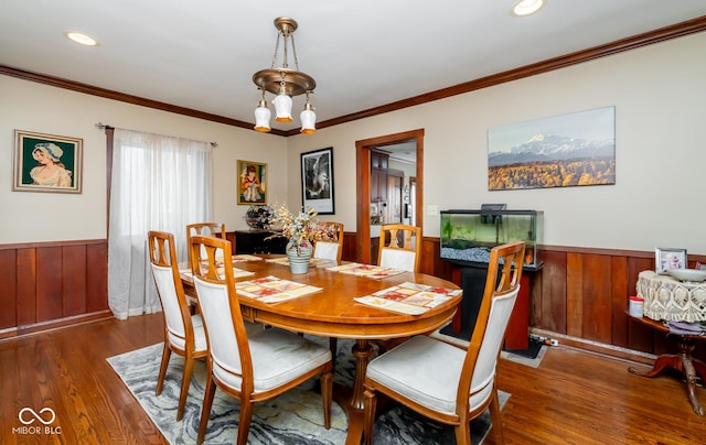 dining area featuring dark wood-style floors, wainscoting, wood walls, and crown molding