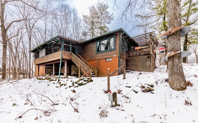 snow covered back of property with a deck and stairway