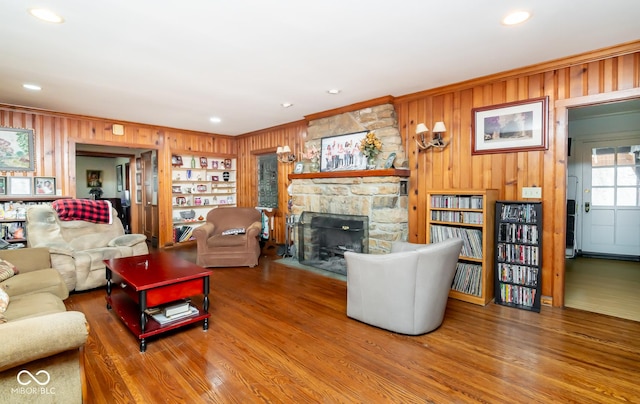 living room with ornamental molding, wood finished floors, a stone fireplace, wood walls, and recessed lighting