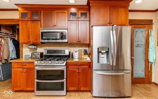 kitchen featuring appliances with stainless steel finishes, glass insert cabinets, and light stone countertops