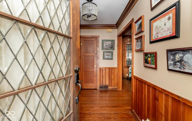 hall featuring dark wood-type flooring, a wainscoted wall, crown molding, and visible vents